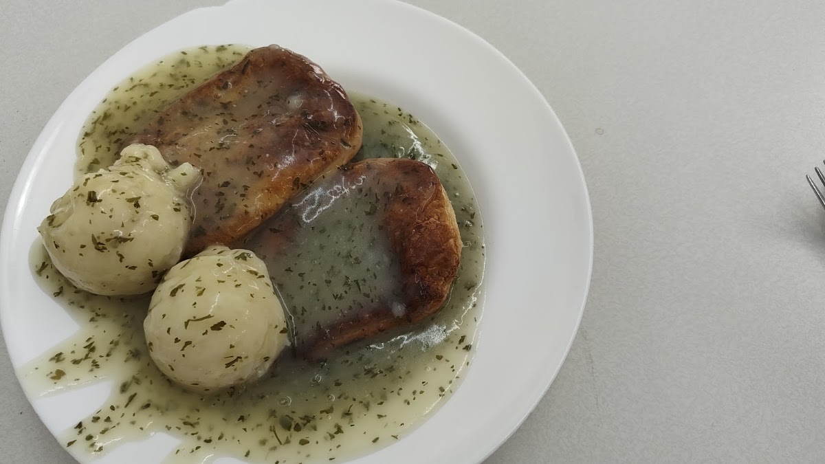 Two pies and two scoops of mashed potato on a white plate, flooded with pale green parsley liquor, on a white formica table.